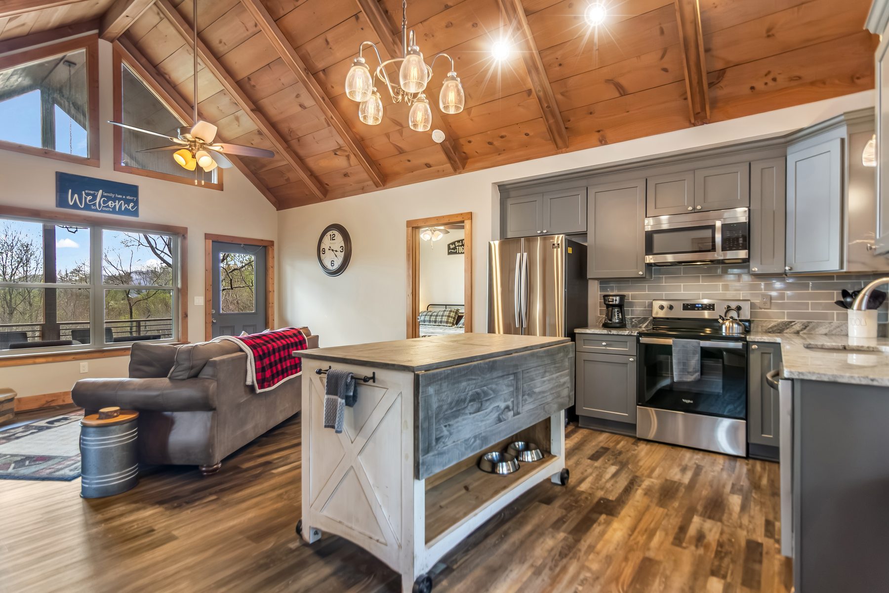 Open-plan kitchen with grey cabinets, butcher-block island, vaulted pine ceiling, and Welcome sign