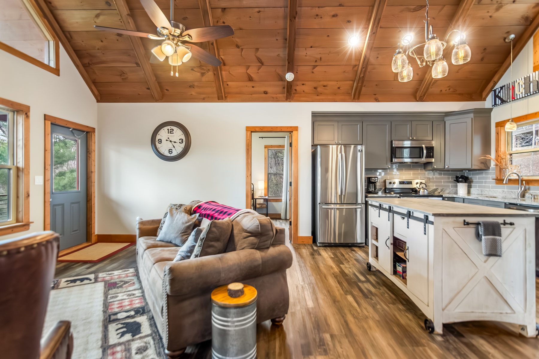 Living area with leather sofa, butcher-block kitchen island, vaulted wood ceilings, and a wall clock