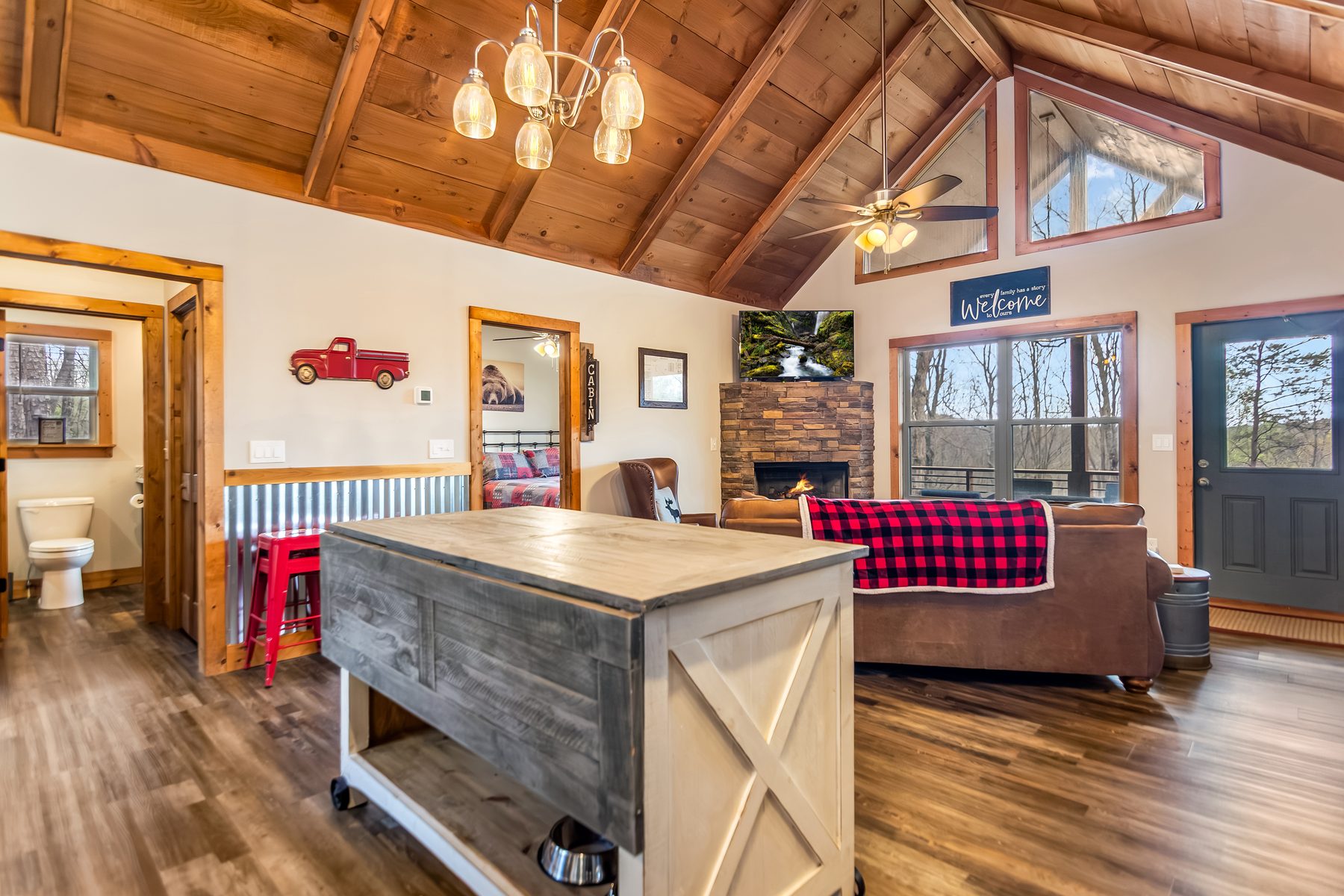 Great room with stone fireplace, plaid throw on the leather sofa, and bedroom doorway