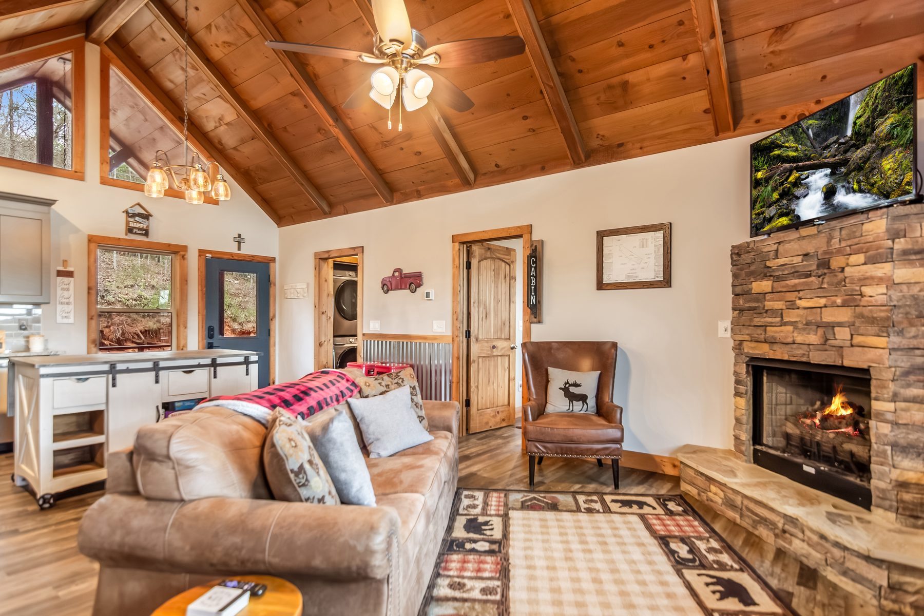 Living room with stone fireplace, leather sofa and wingback chair, area rug, and mounted TV