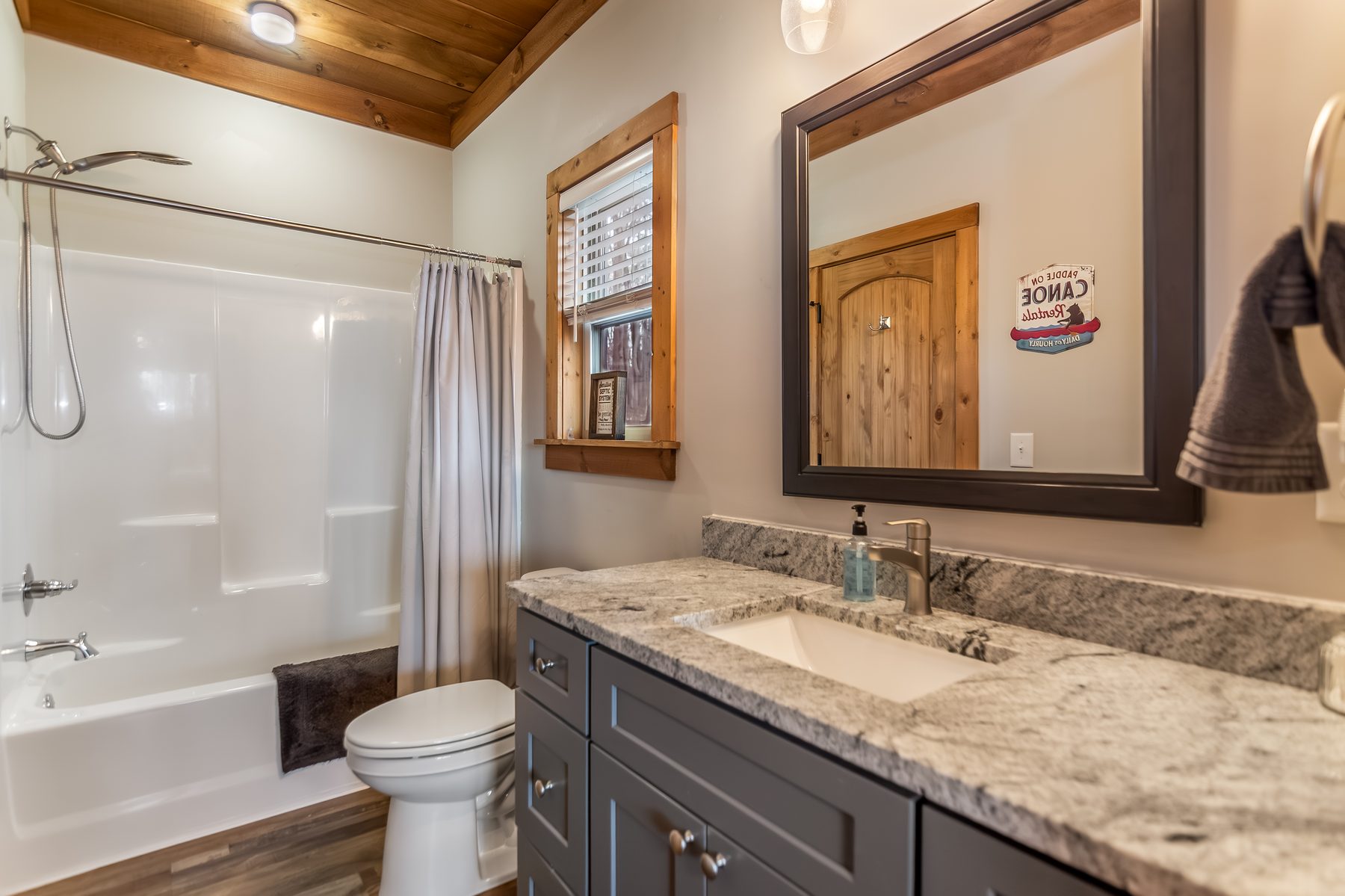 Bathroom with shower-tub combo, granite vanity, and Saddle Up canoe-rental sign