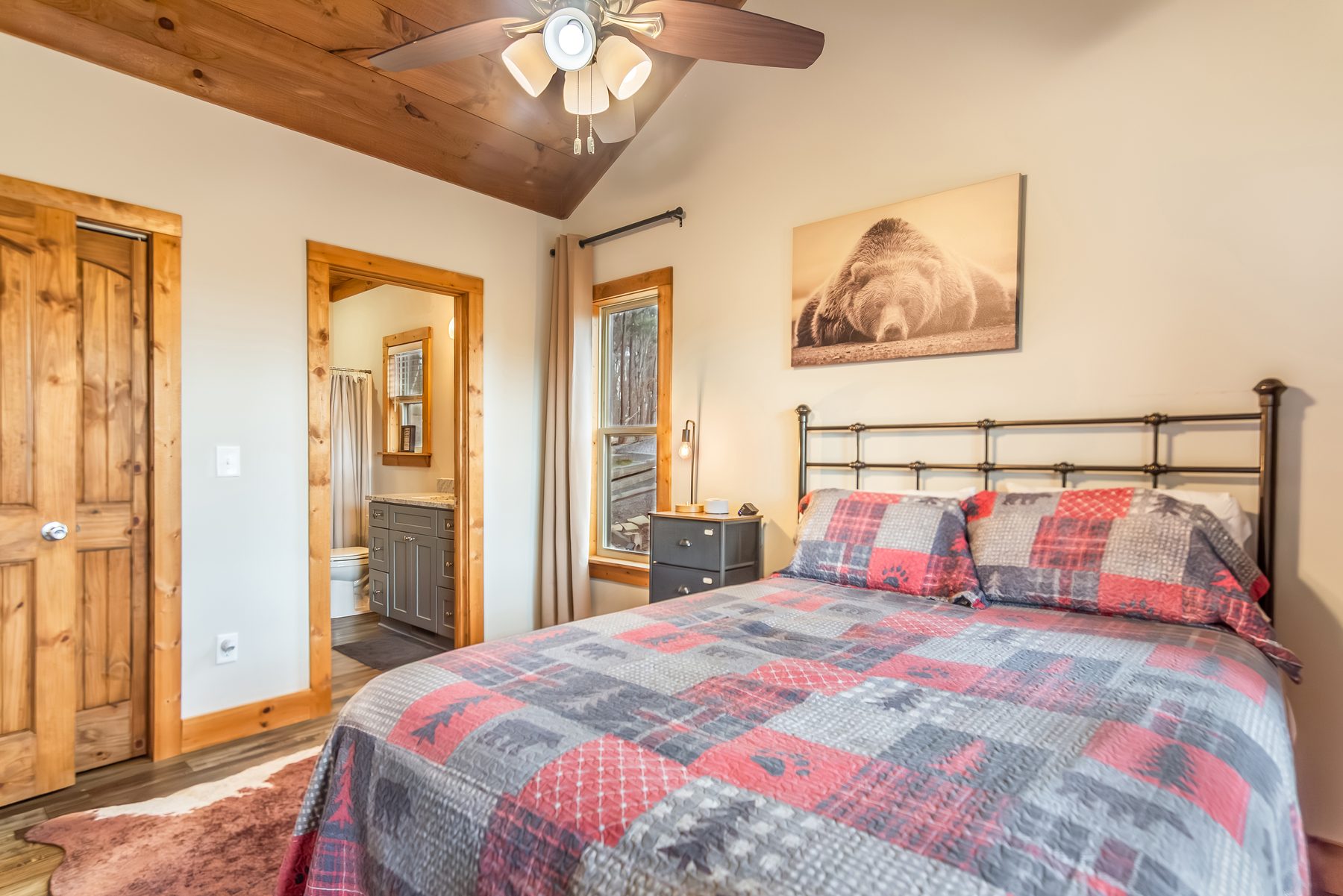 Queen bedroom with plaid quilt, sleeping-bear print, and en-suite bath visible