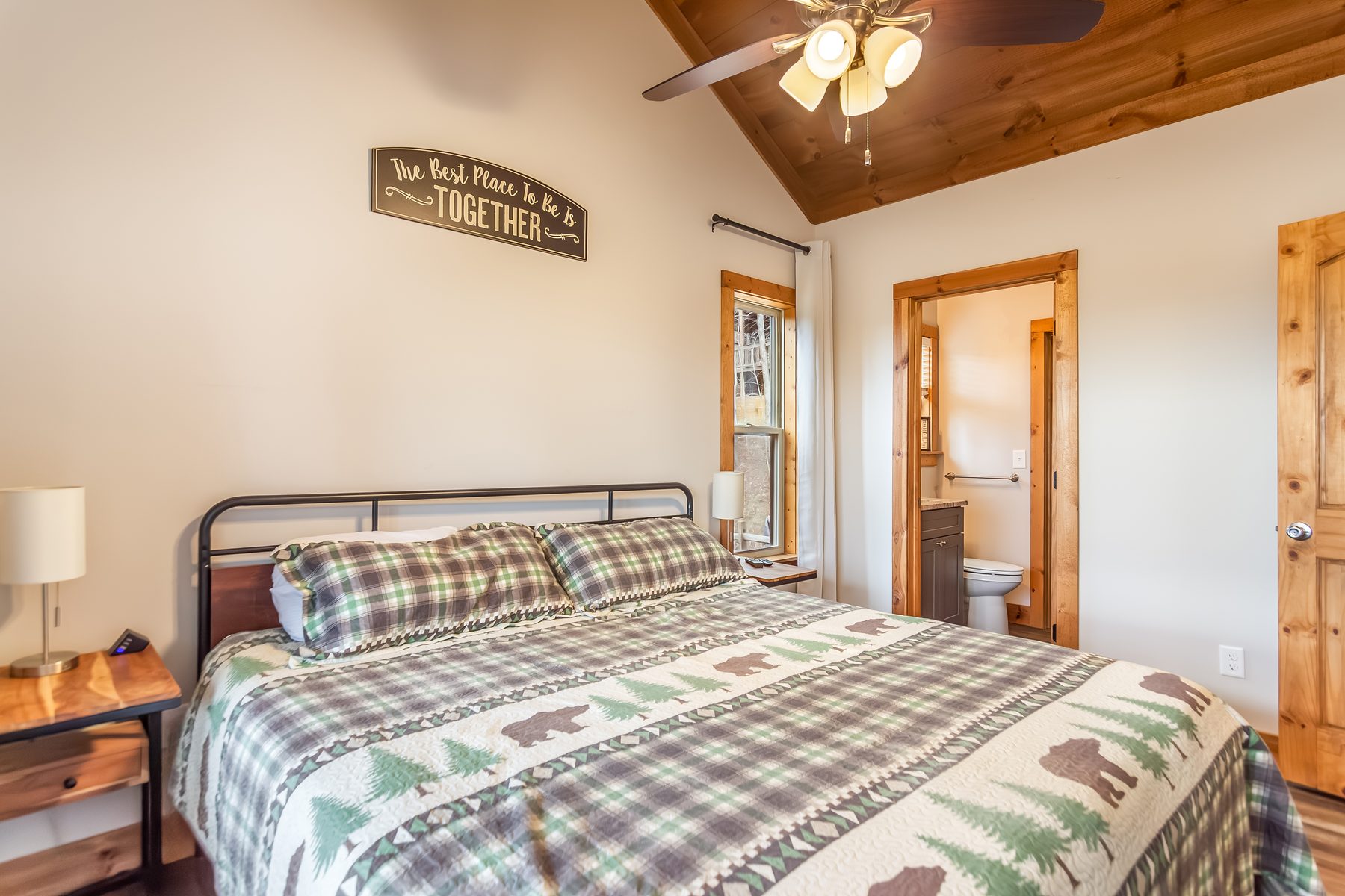 Queen bedroom with plaid bear quilt, Best Place to Be is Together sign, en-suite bath visible