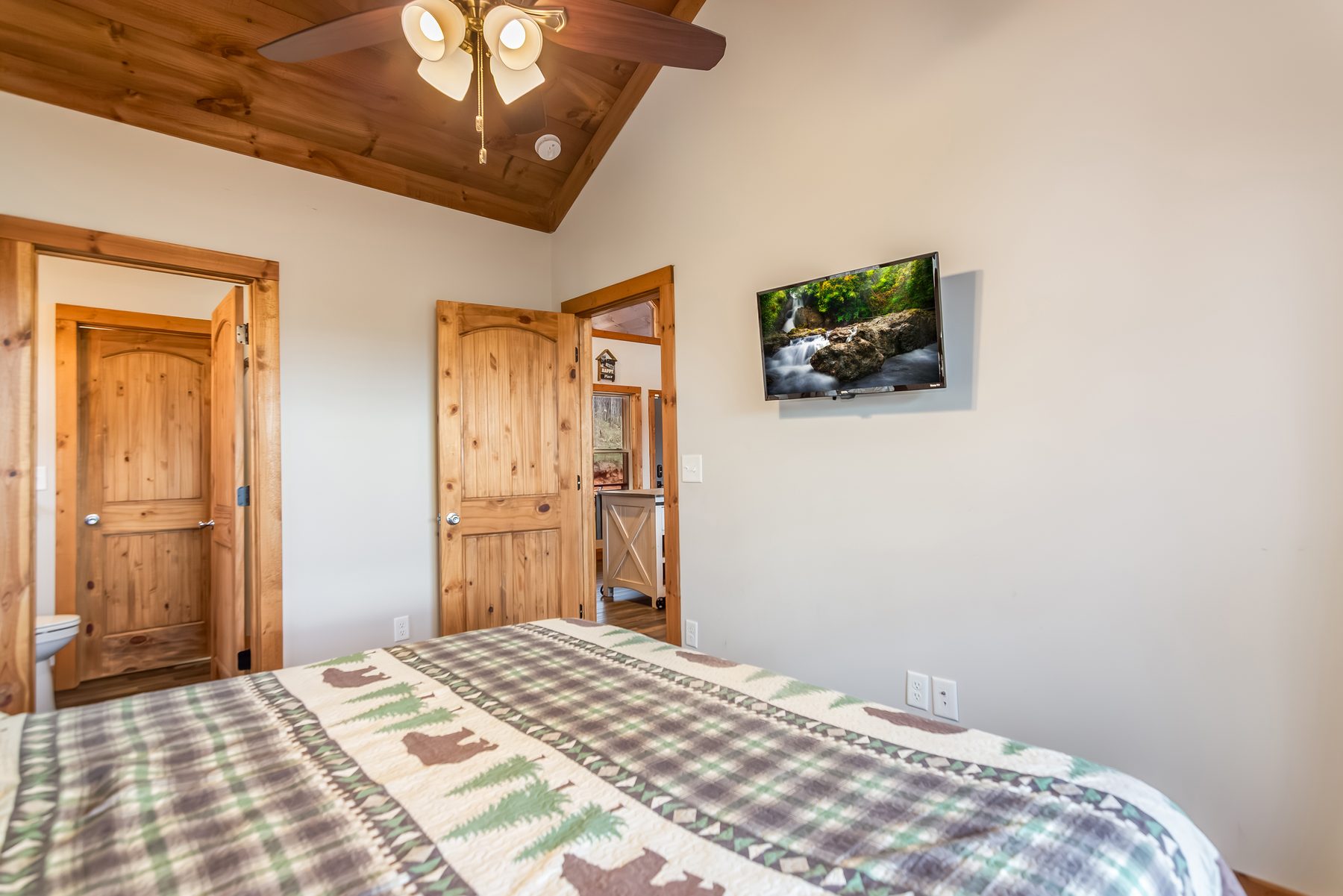 Bedroom with mounted TV showing a waterfall scene and doorways to the bath and great room