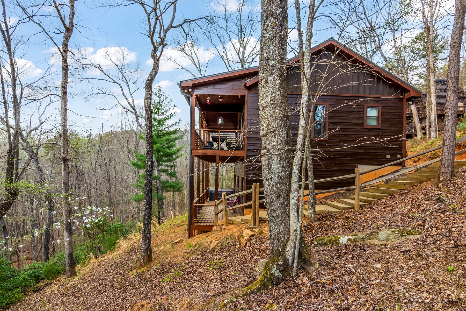 Cabin exterior side view set into the spring woods, with wraparound deck